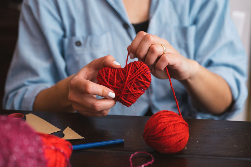 A person creating a red yarn heart, showcasing the process of handcrafting.